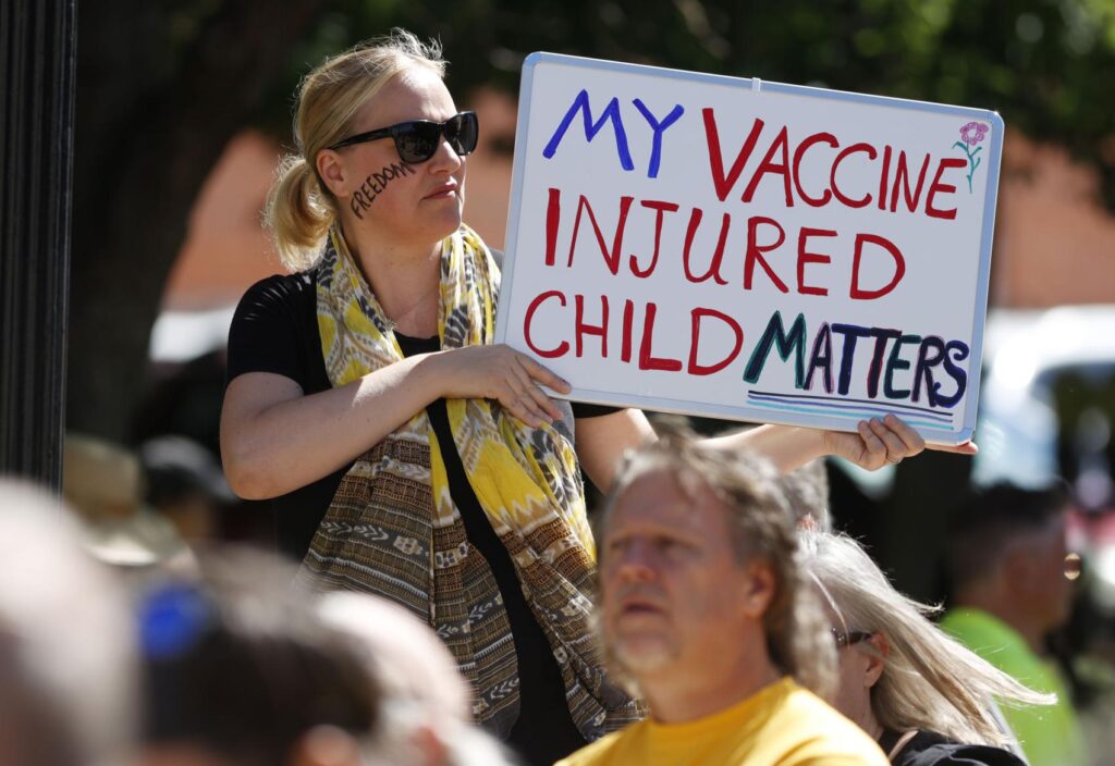 Simone Warstat of Louisville, Colo., waves a placard during a rally against a legislative bill to make it more difficult for parents to opt out for non-medical reasons to immunize their children Sunday, June 7, 2020, in Denver. 